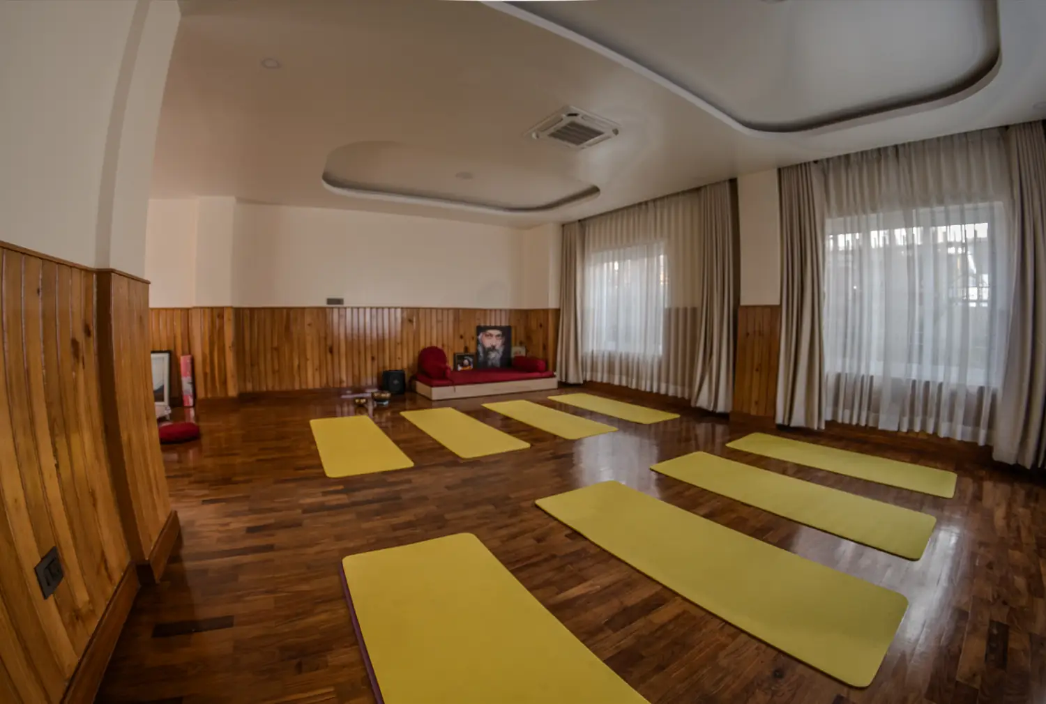 Meditation hall with rows of yellow mats and a low platform with red cushions
